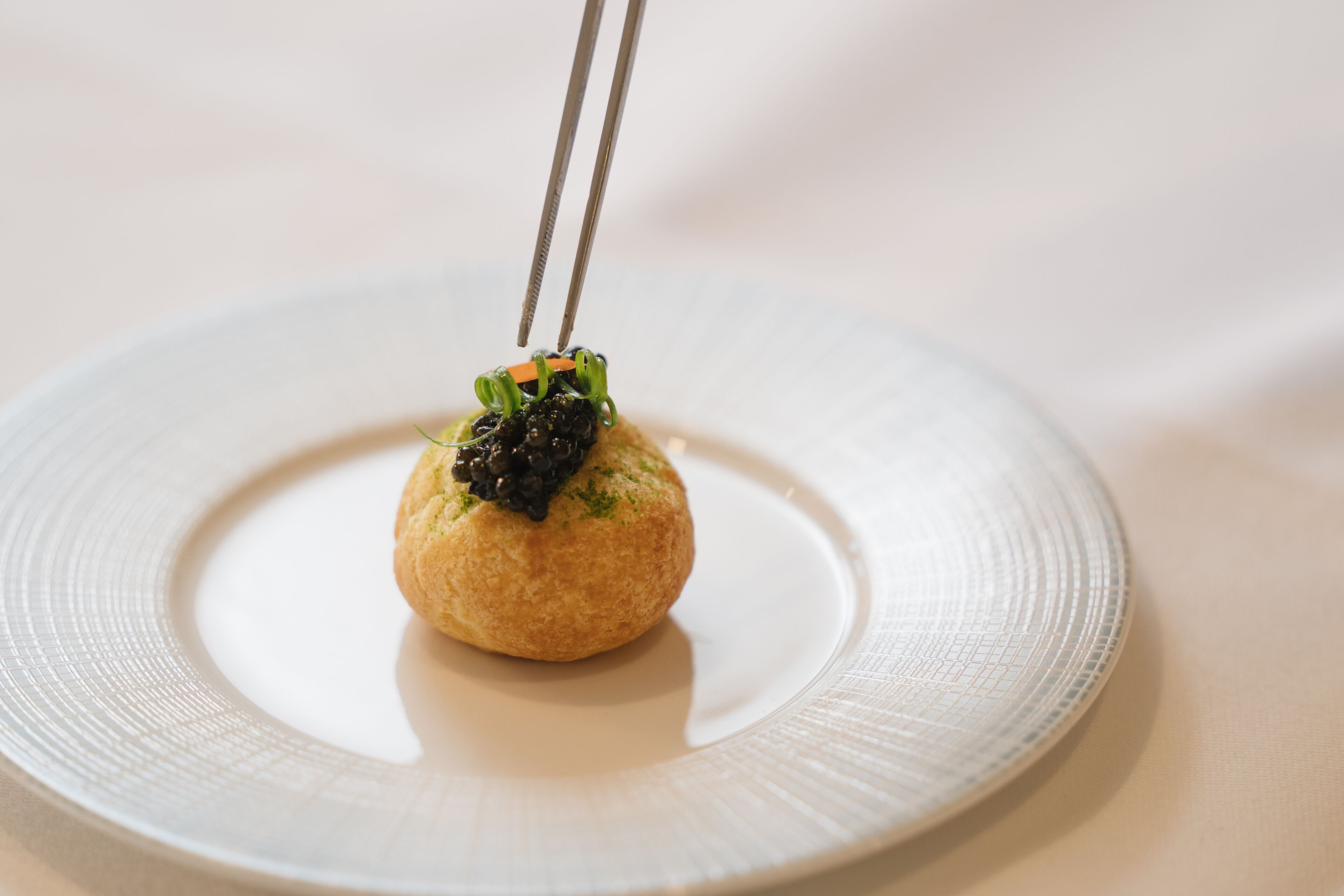 A round plate with a small, round food item on top, held by chopsticks.
