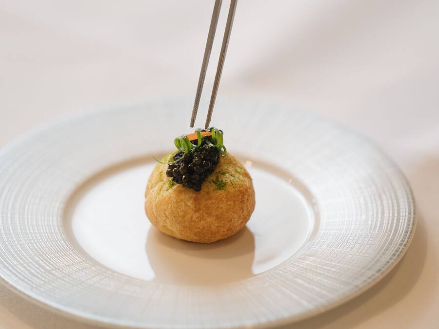 A round plate with a small, round food item on top, held by chopsticks.