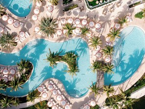 Vue aérienne d’un complexe hôtelier doté de plusieurs piscines, de chaises longues et de palmiers.