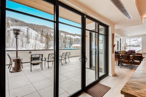 A modern interior with large sliding glass doors leading to a balcony with a view of a snowy mountain landscape. - Ski Club Penthouse (Vail)