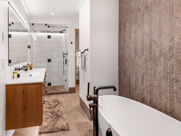 A modern bathroom with a white bathtub, a large mirror, a shower area, and a wooden vanity. - Red Lion Penthouse (Vail)