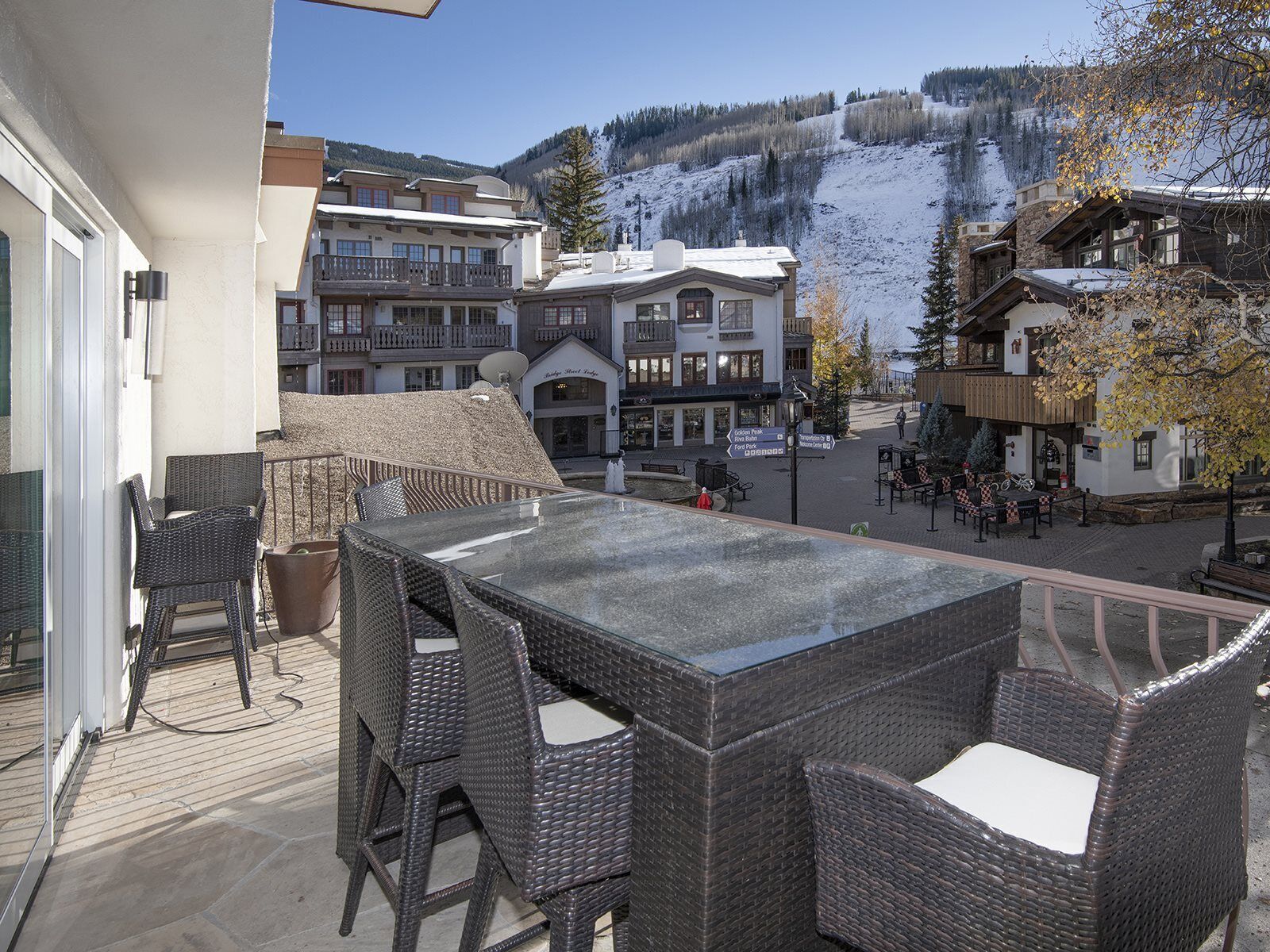 A balcony with wicker furniture, a view of a snowy mountain, and buildings in the background.