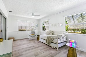 Relax in a spacious room with a high ceiling, featuring a comfortable bed, seating area, and large windows with a view of lush greenery.