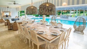 Ein Essbereich mit einem großen Holztisch, gedeckt für sechs Personen, umgeben von Korbstühlen, mit Pool und Sitzgelegenheiten im Hintergrund.