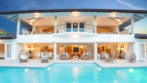 Ein zweistöckiges Haus mit Swimmingpool, Sitzgelegenheiten im Freien und einem Balkon.