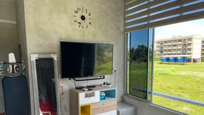 A room with a large window, a flat-screen TV, a small refrigerator, and a wall clock. - OYO Home 90370 D'tampi Homestay (Semporna)