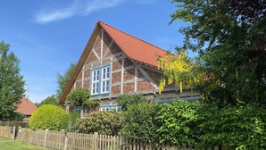 A traditional half-timbered house with a red-tiled roof, surrounded by a wooden fence and lush greenery. - Spacious room for two (Dömitz OT Rüterberg)