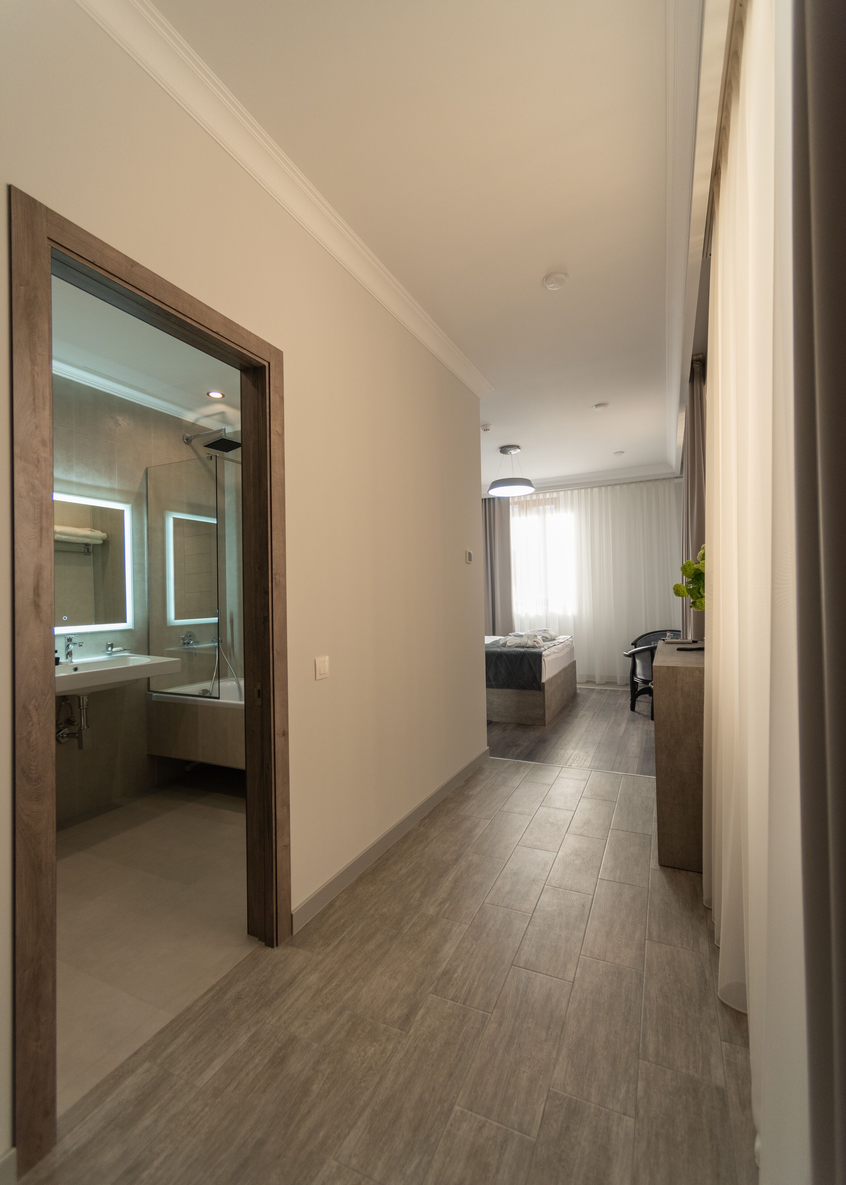 A modern hotel room with a large mirror, a separate bathroom, a bed, and a small seating area.