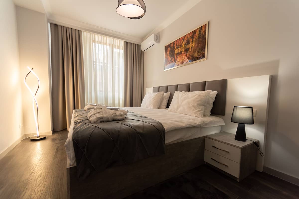 A modern hotel room with a large bed, a bedside table, a lamp, and a painting on the wall.