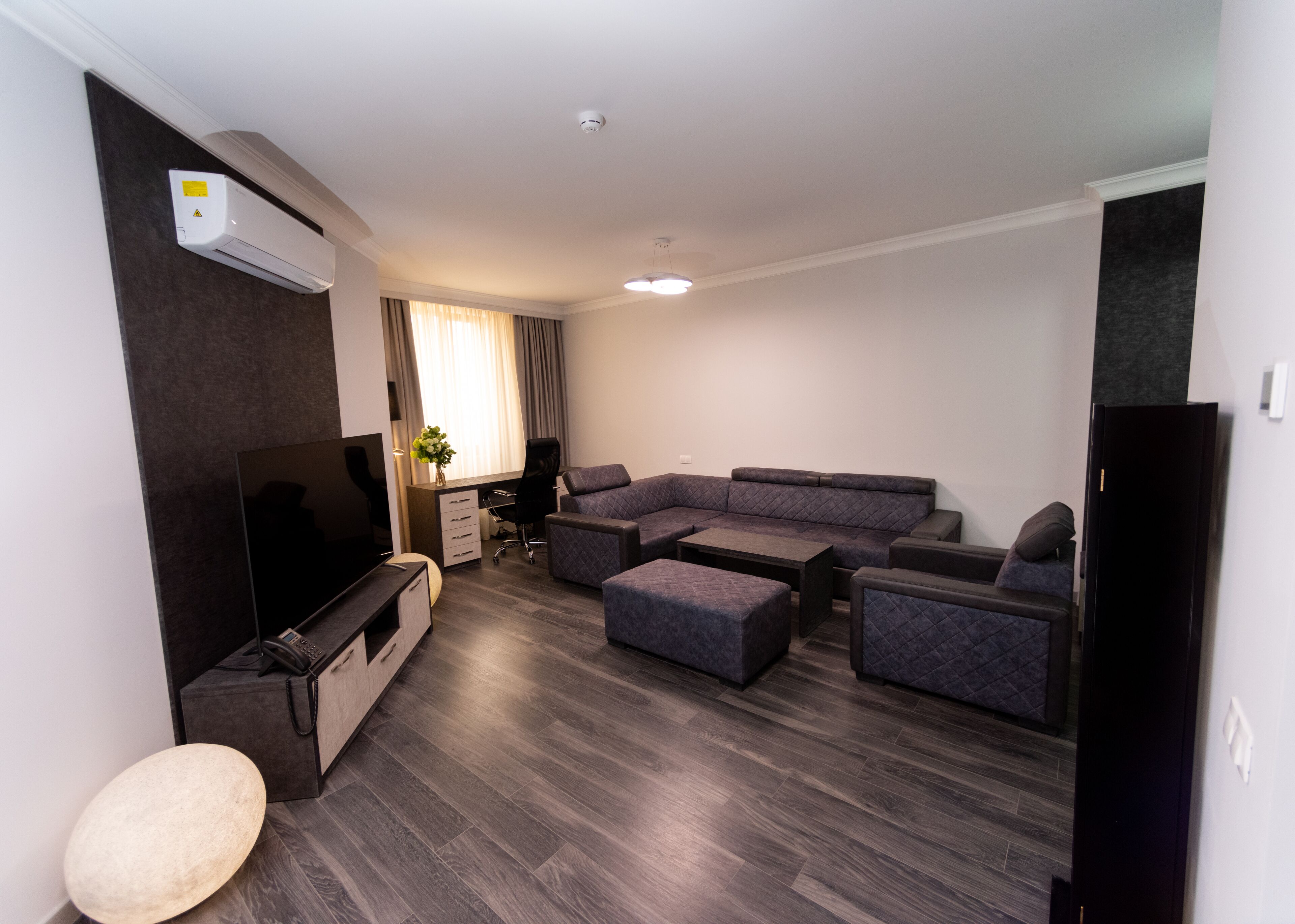 A modern living room with a sectional sofa, a flat-screen TV, a desk, and a small side table.