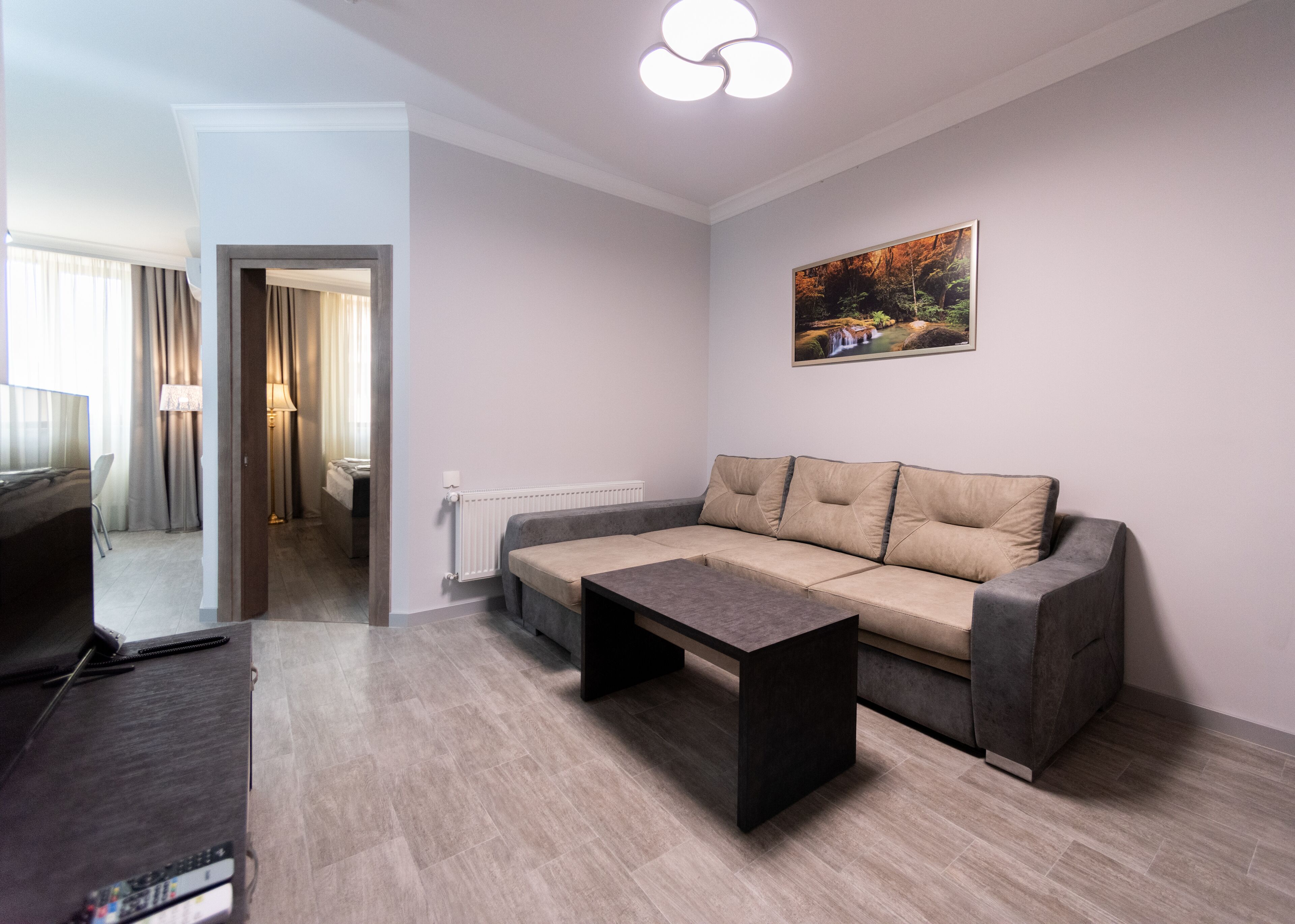 A modern living room with a sofa, a coffee table, and a TV. There is a painting on the wall and a lamp in the corner.