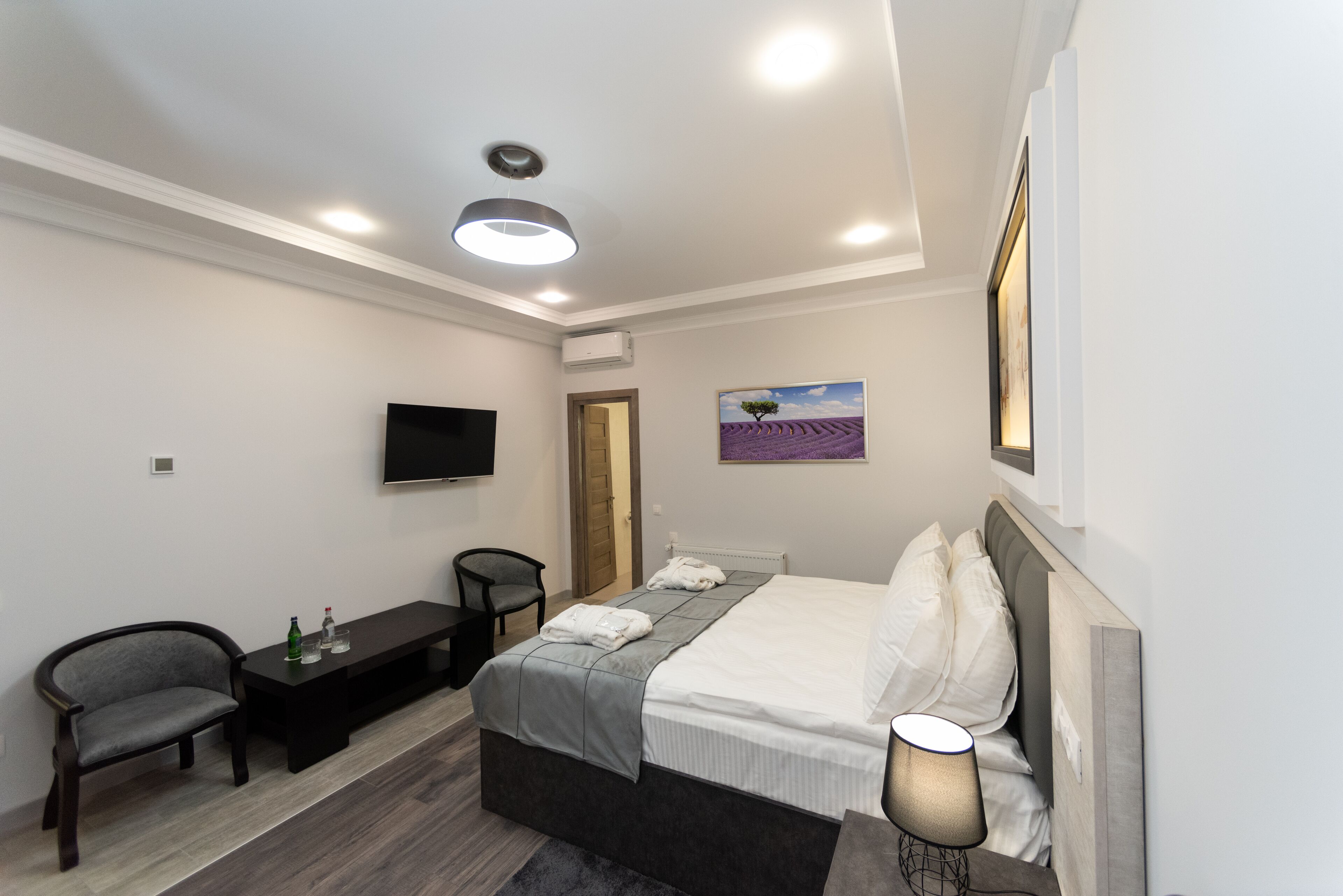A modern hotel room with a bed, a desk, a chair, a TV, and a painting on the wall.