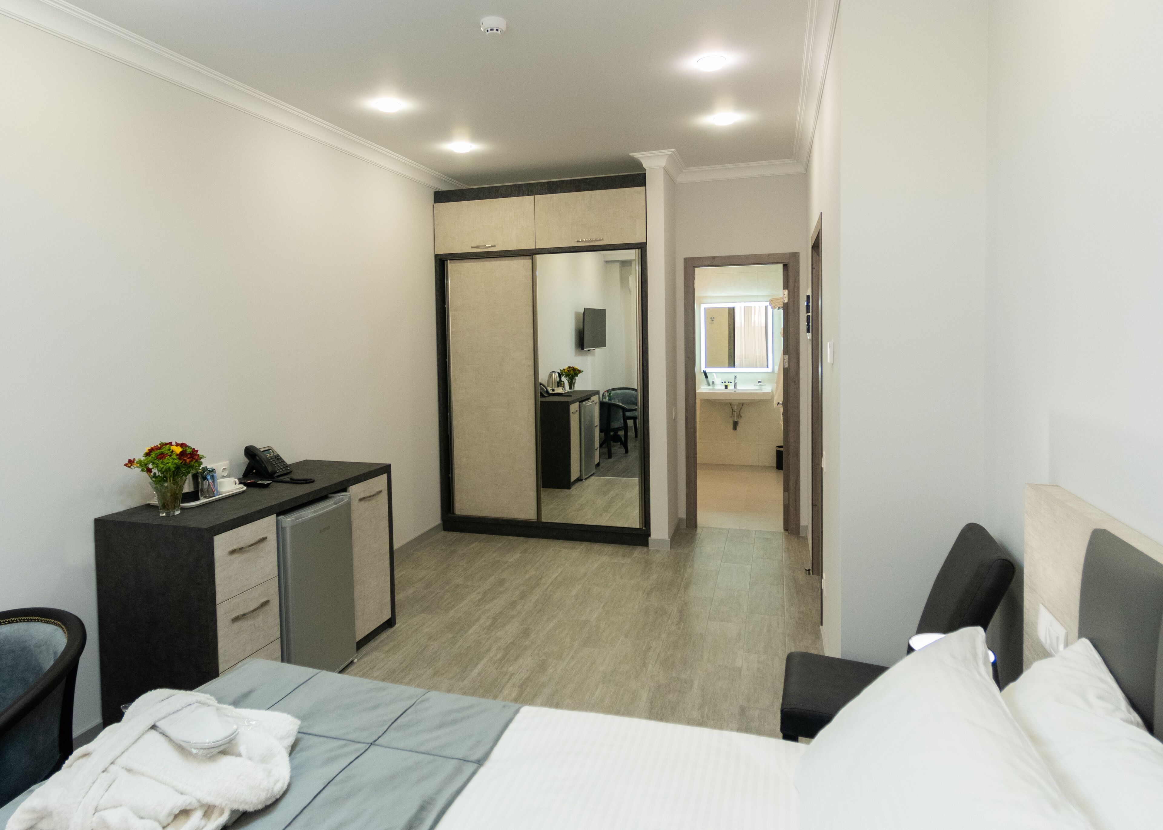 A hotel room with a bed, bedside table, desk, and a mirror.