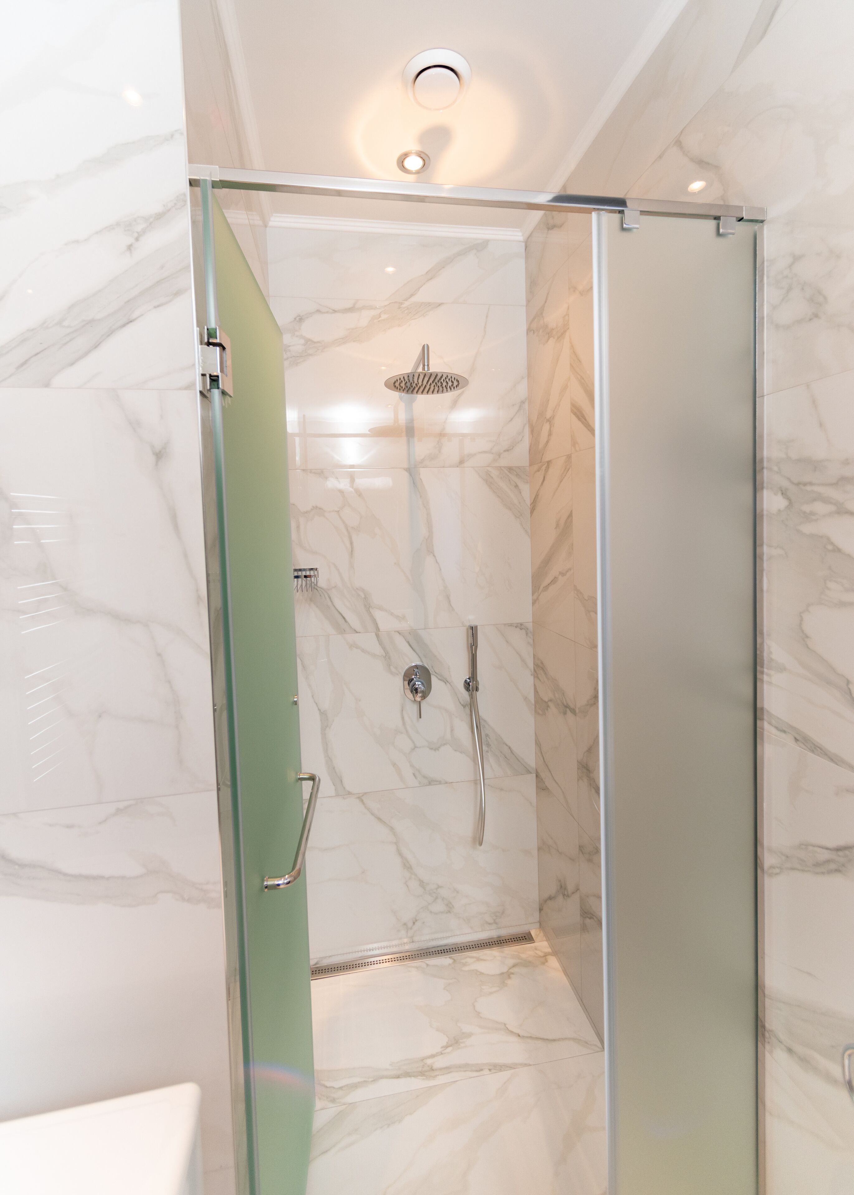 A glass-enclosed shower with a handheld showerhead and a wall-mounted faucet.