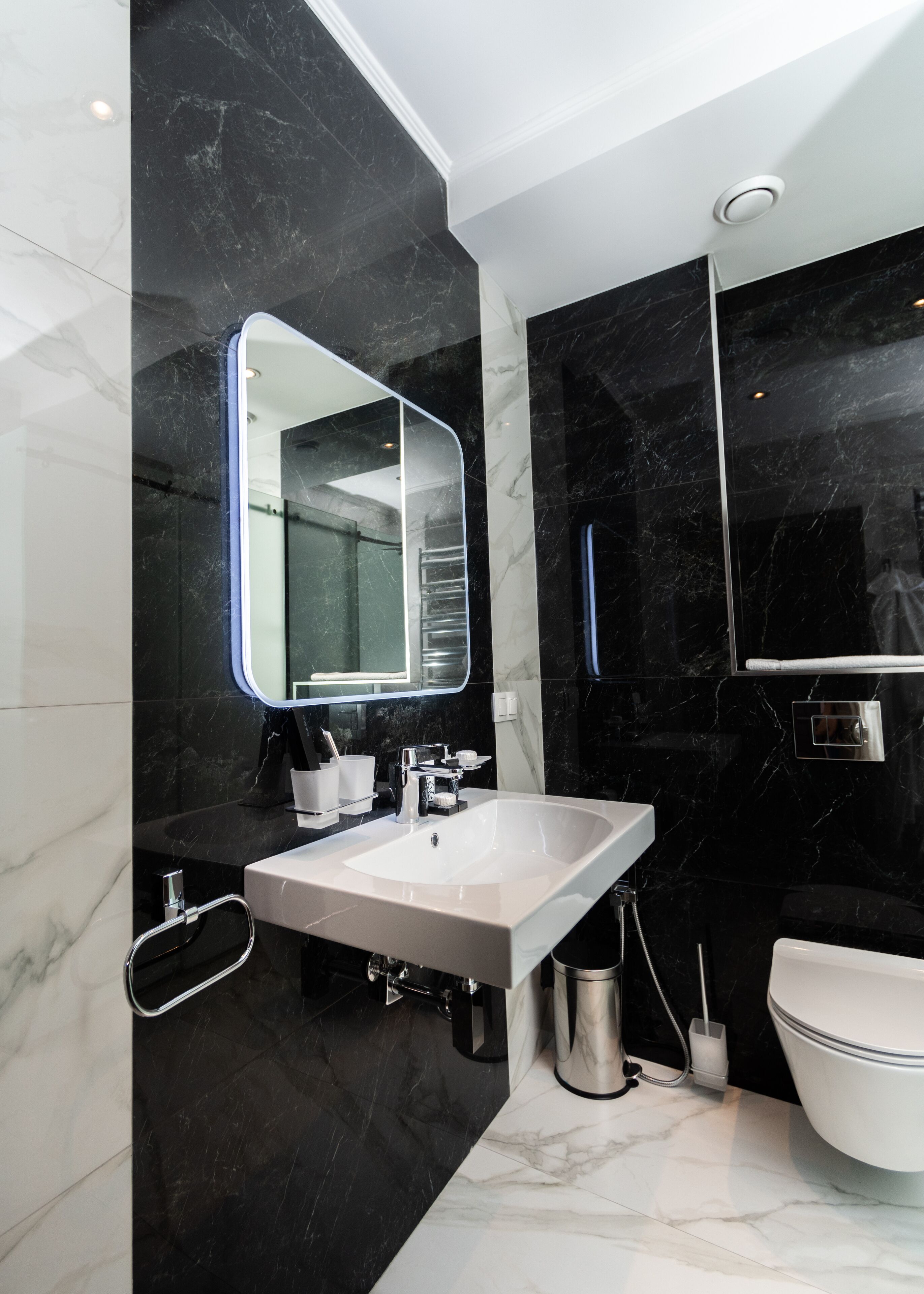 Un baño moderno con un espejo grande, un lavamanos blanco y un inodoro.