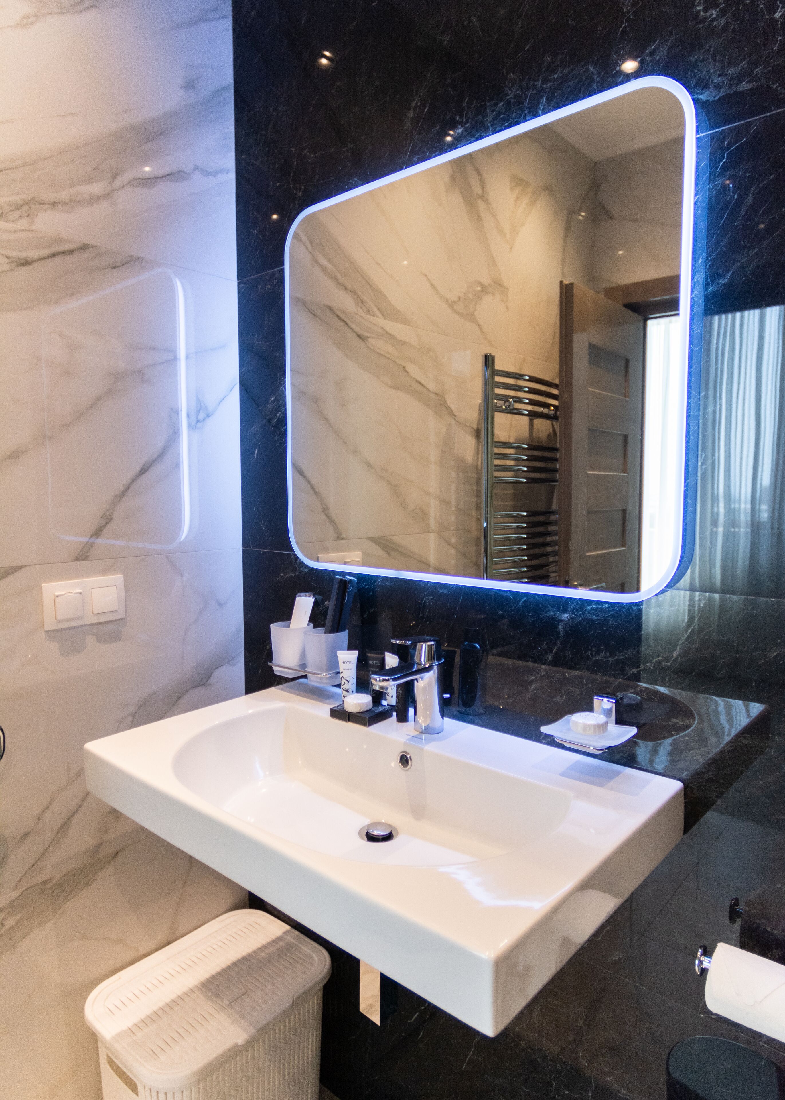 A modern bathroom with a large mirror, white sink, and dark marble walls.