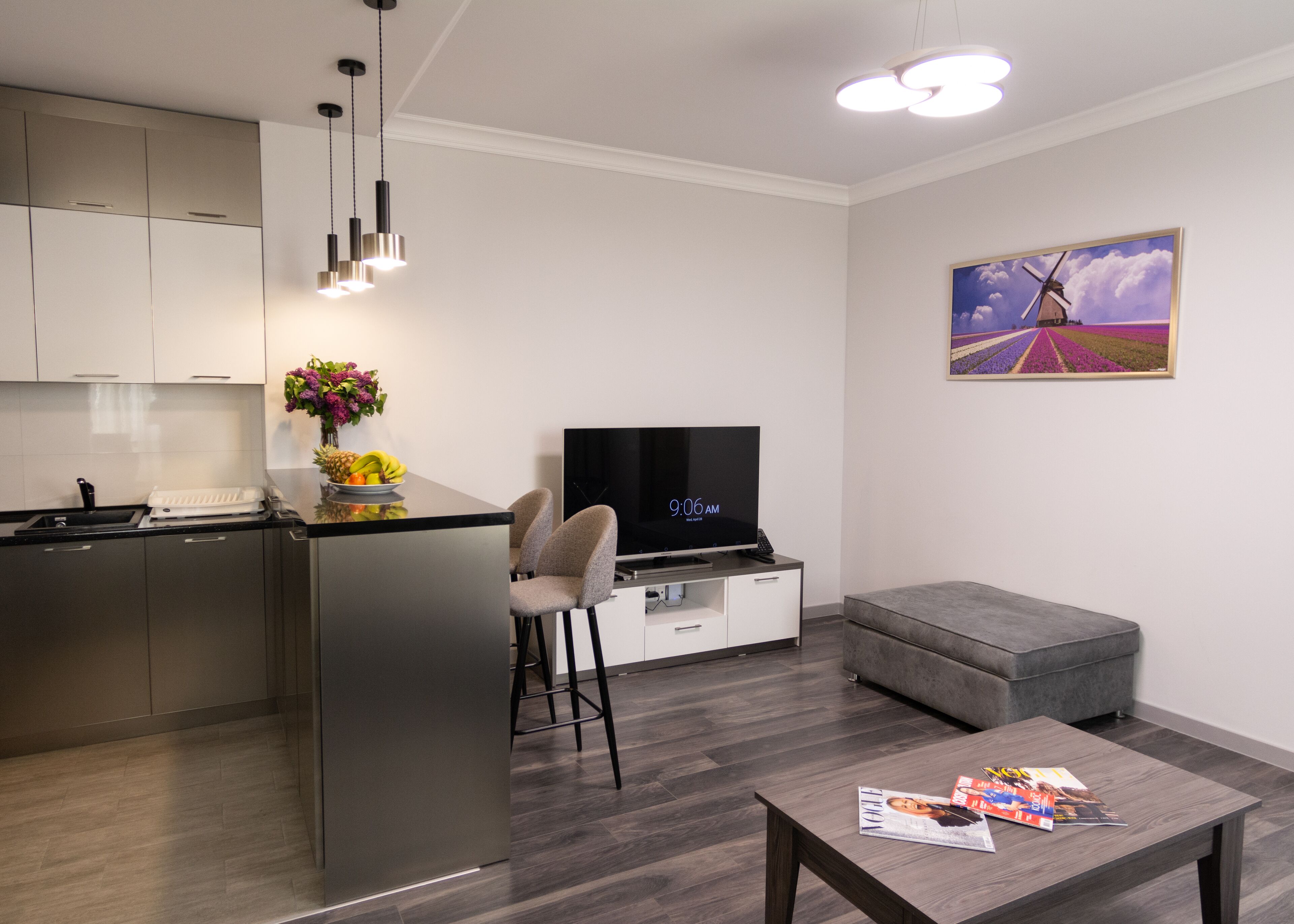 A modern kitchen with a central island, a dining area with a TV, and a living space with a sofa and a magazine on a coffee table.
