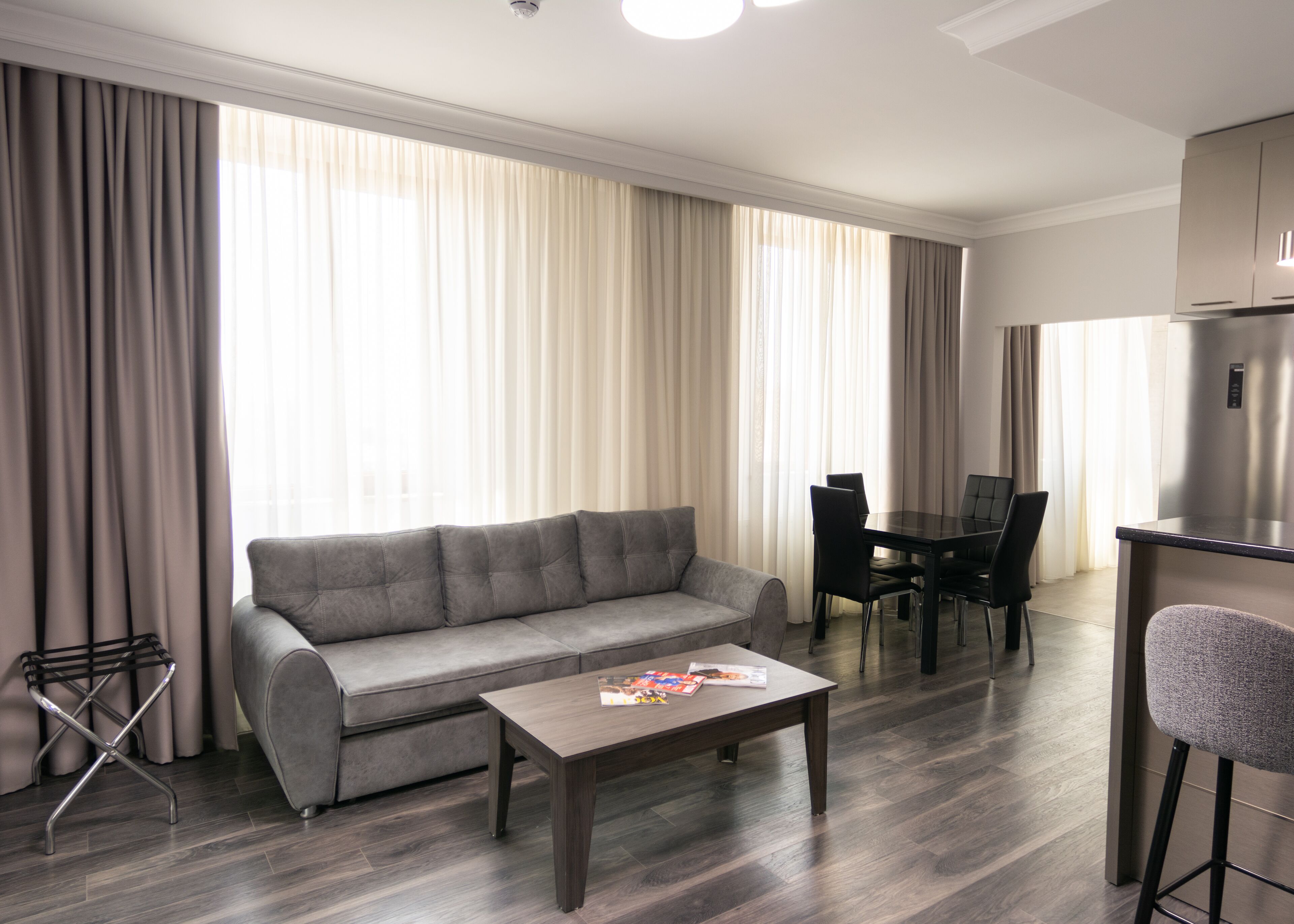 A modern living room with a grey sofa, a wooden coffee table, and a dining area with a black table and chairs.