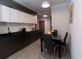 Een moderne keuken met donkere kastjes, een zwart aanrechtblad, en een eethoek met een tafel en stoelen.