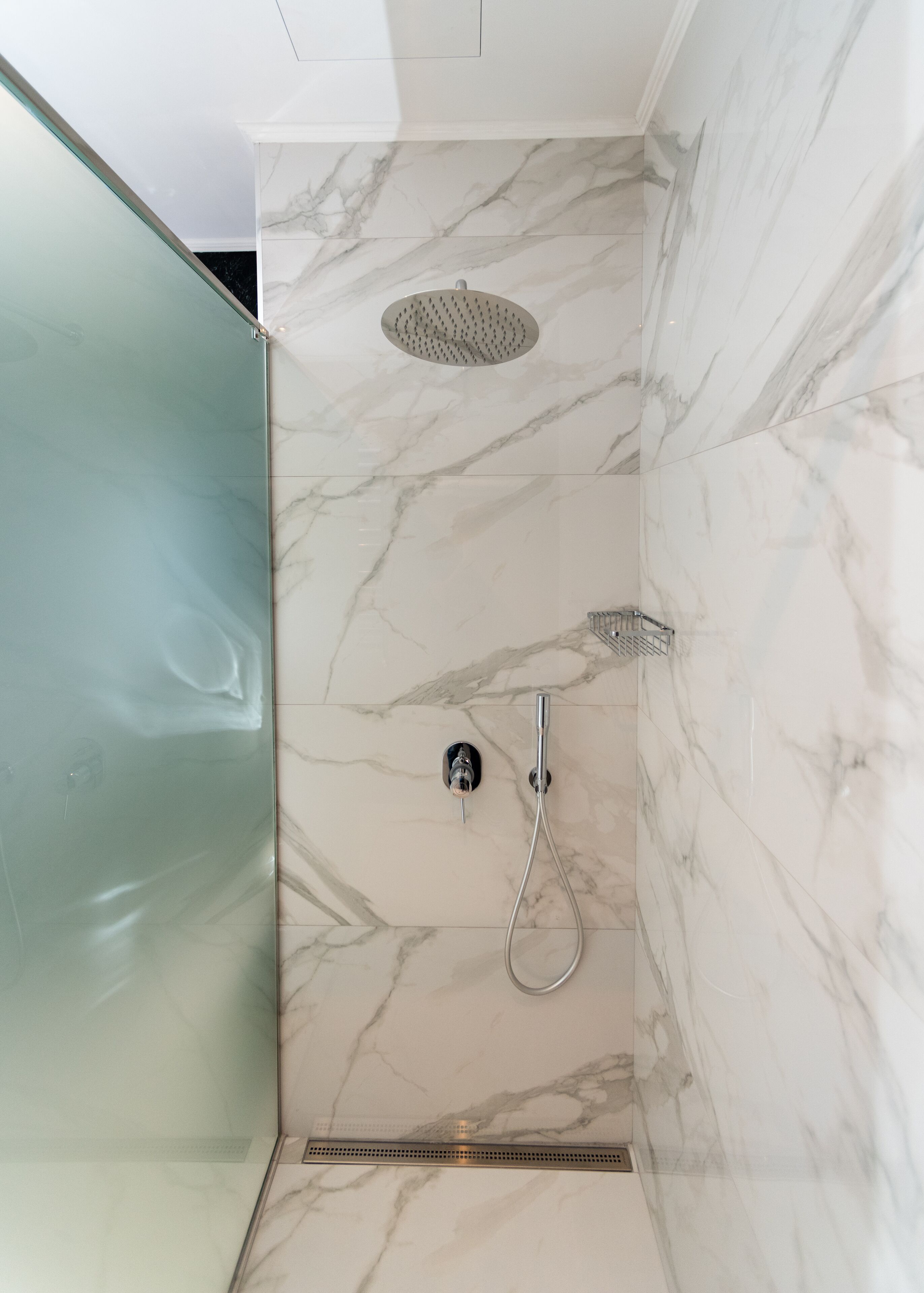Een moderne badkamer met een douchecabine van glas, een handdouche en een muurbevestigde kraan.