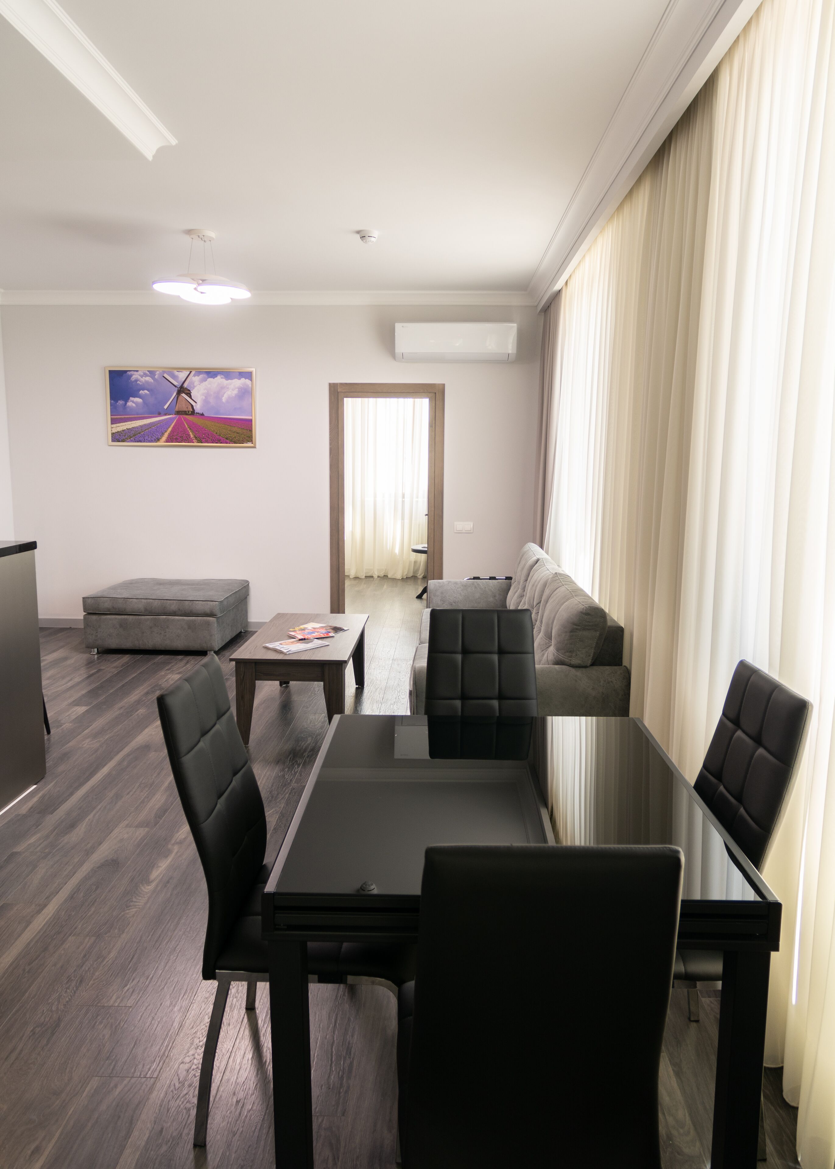 Una sala de estar moderna con una mesa de comedor de vidrio, sillas de cuero negro, un sofá gris y un cuadro de un molino.
