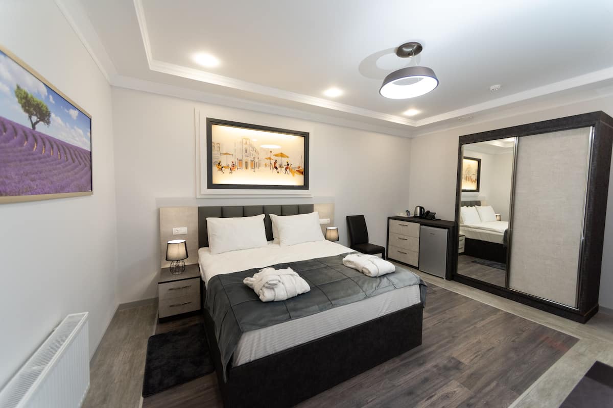 A modern hotel room with a large bed, bedside tables, a mirror, and artwork on the walls.