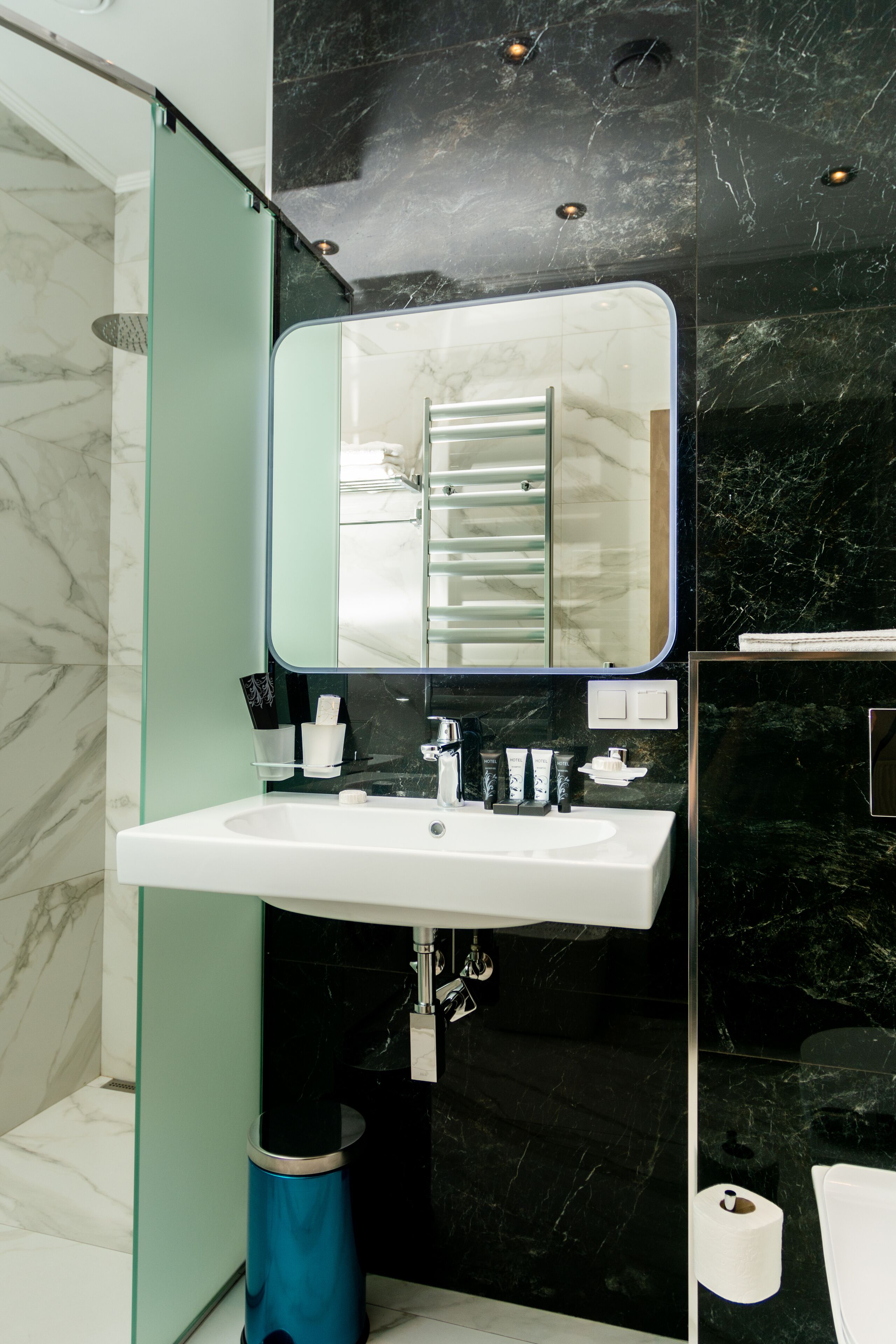 A modern bathroom with a white sink, black marble walls, and a glass shower enclosure.