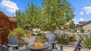 Un patio con sillas Adirondack, un hogar de piedra y vista a un barrio residencial.