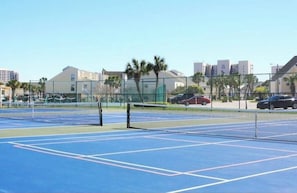 Un court de tennis en plein air, doté d’un filet, entouré d’une clôture et bordé de palmiers.