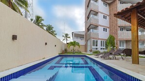 A swimming pool with blue tiles, surrounded by a beige wall and a brick building. - Apart Porto de Galinhas para 4 pessoas (Ipojuca)