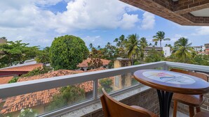 A balcony with a view of a cityscape, including palm trees and buildings with red-tiled roofs. - Apart Porto de Galinhas para 4 pessoas (Ipojuca)