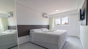 A modern hotel room with a large bed, a bedside table, a mirror, and a window with a view of the city. - Apart Porto de Galinhas para 4 pessoas (Ipojuca)