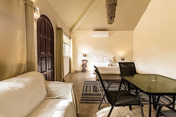 Une chambre d’hôtel comprenant un lit, une table à manger avec des chaises, un canapé, une lampe et un appareil de climatisation.