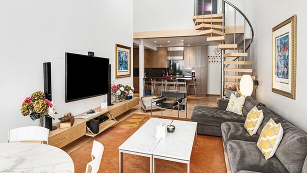 A modern living room with a flat-screen TV, a sofa, a coffee table, and a staircase. - Lionshead Center (Vail)