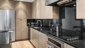 A modern kitchen with stainless steel appliances, wooden cabinets, and a black countertop. - Lionshead Center (Vail)