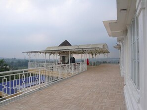 Un balcón con zona de estar cubierta, barandilla blanca y vistas al paisaje.