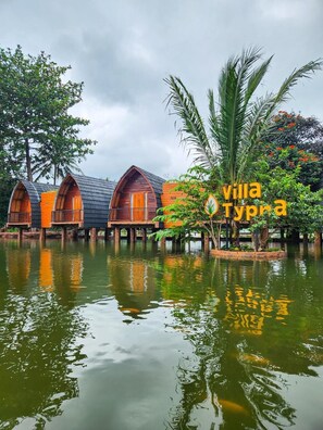 A waterfront property with wooden overwater bungalows, a sign reading 'villa Typha,' and a calm water body reflecting the structures. - Chevilly Resort And Camp (Ciawi)