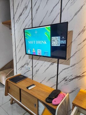 Habitación de hotel con pared de mármol, televisor de pantalla plana montado en la pared, escritorio de madera con teléfono y un teléfono celular plegable, y un par de pantuflas en el suelo.