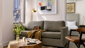 A modern living room with a grey sofa, a wooden coffee table, a vase with green plants, and a framed abstract painting on the wall.