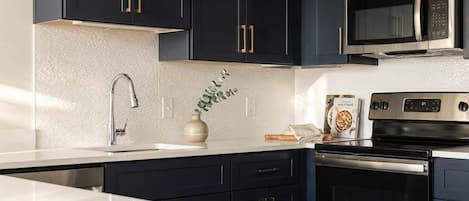 Cocina moderna con armarios oscuros, electrodomésticos de acero inoxidable y encimera blanca.