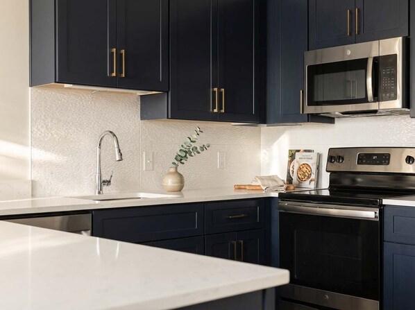 A modern kitchen with dark cabinets, stainless steel appliances, and a white countertop.