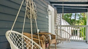 A porch with a hanging white macrame chair, a wicker chair, and a table with a patterned rug. - 724A · The Blue Bungalow - Min to Downtown and Airport! (Atlanta)