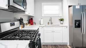 A modern kitchen with white cabinets, a stainless steel refrigerator, a microwave, and a gas stove. - 724A · The Blue Bungalow - Min to Downtown and Airport! (Atlanta)