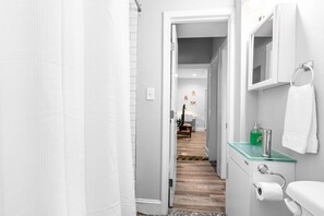 Bathroom features a glass shower enclosure, white toilet, and sink with a soap dispenser.