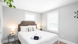 A neatly made bed with a headboard, a bedside table with a lamp, and a wall clock. - 724A · The Blue Bungalow - Min to Downtown and Airport! (Atlanta)
