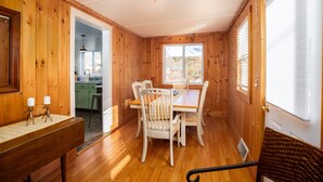 A wooden interior with a dining table and chairs, a kitchen area, and a window with blinds. - The Lodge House - Centrally Located Cheerful 5BR - Minutes to Gore! (North Creek)