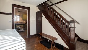 A wooden staircase with a bench at the bottom, leading to a second floor. A kitchen is visible through an open door in the background. - The Lodge House - Centrally Located Cheerful 5BR - Minutes to Gore! (North Creek)