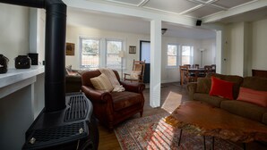 A living room with a fireplace, a brown leather armchair, a patterned rug, and a sofa with red cushions. - The Lodge House - Centrally Located Cheerful 5BR - Minutes to Gore! (North Creek)