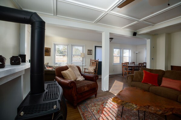 A living room with a fireplace, a brown leather armchair, a patterned rug, and a sofa with red cushions.