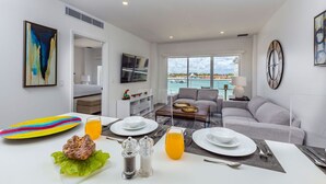 A modern living room with a dining area, a sofa, a TV, and a view of the sea. - Where Comfort Meets Convenience (Oranjestad)